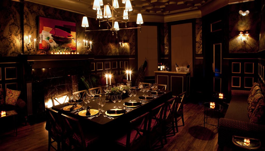 An elegant dinner party setup in NYC featuring a long table with lit candles, fine china, and a cozy fireplace in a room with traditional decor.