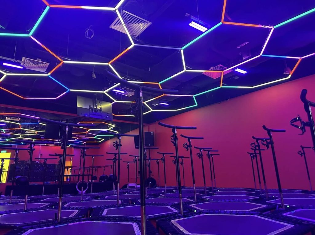 An empty trampoline park with colourful neon lights on the ceiling and fitness equipment.