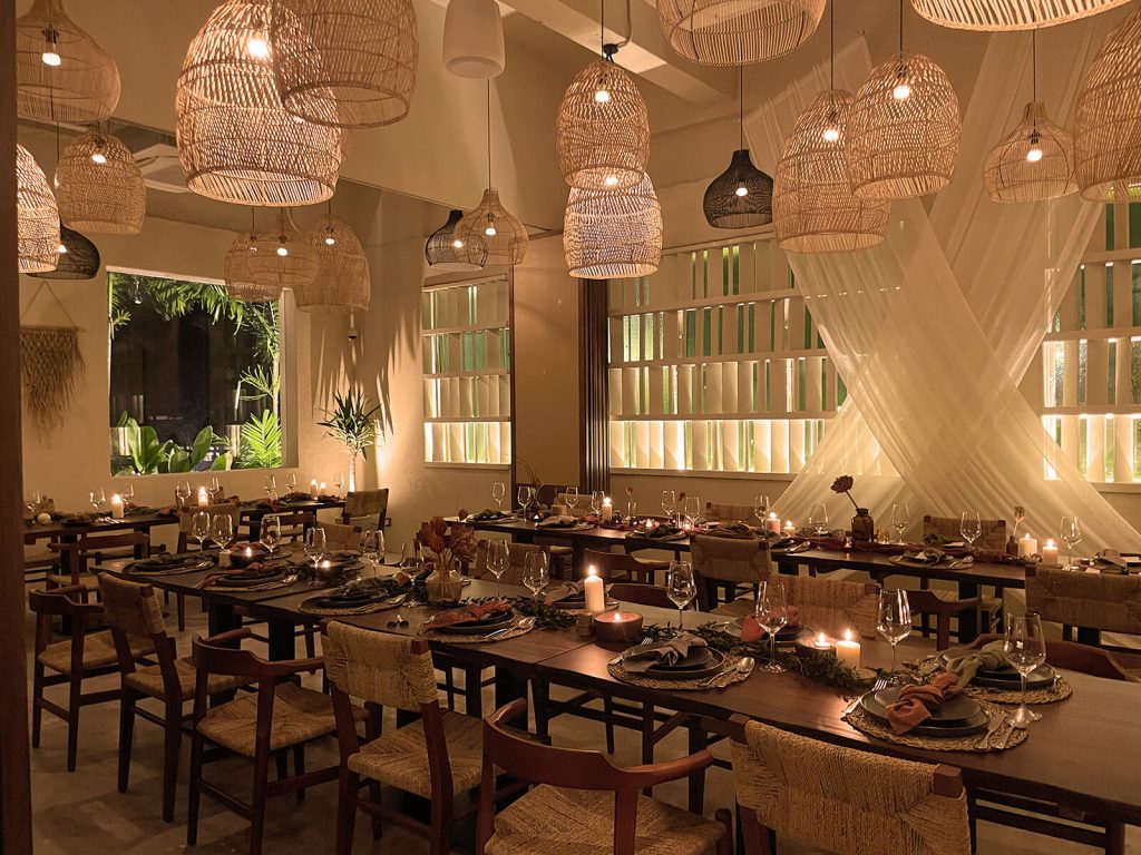 An elegantly set dining room with hanging wicker lamps and a tropical view through the windows.