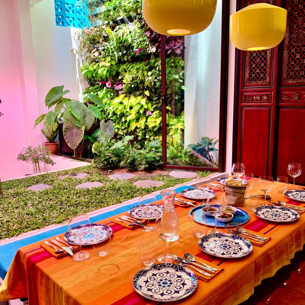 A dining table set for a meal with vibrant colours and an indoor garden in the background.