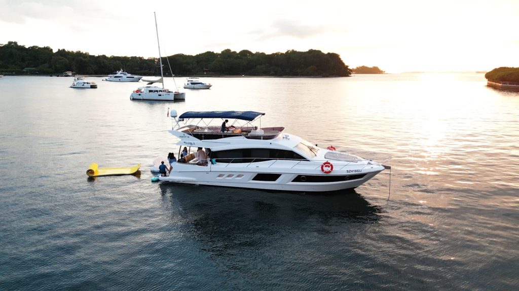 Aerial view of a yacht on calm waters at sunset with other boats nearby and a coastline in the distance.