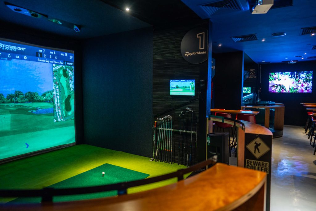 Indoor golf simulator bay with a large screen displaying a virtual golf course, part of a sports club in Singapore.