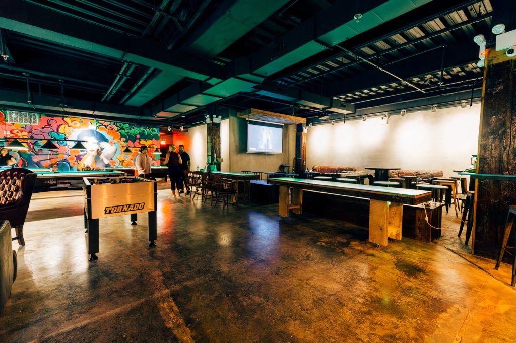 An energetic indoor game room with people playing foosball and billiards, ideal for fun group activities in NYC.