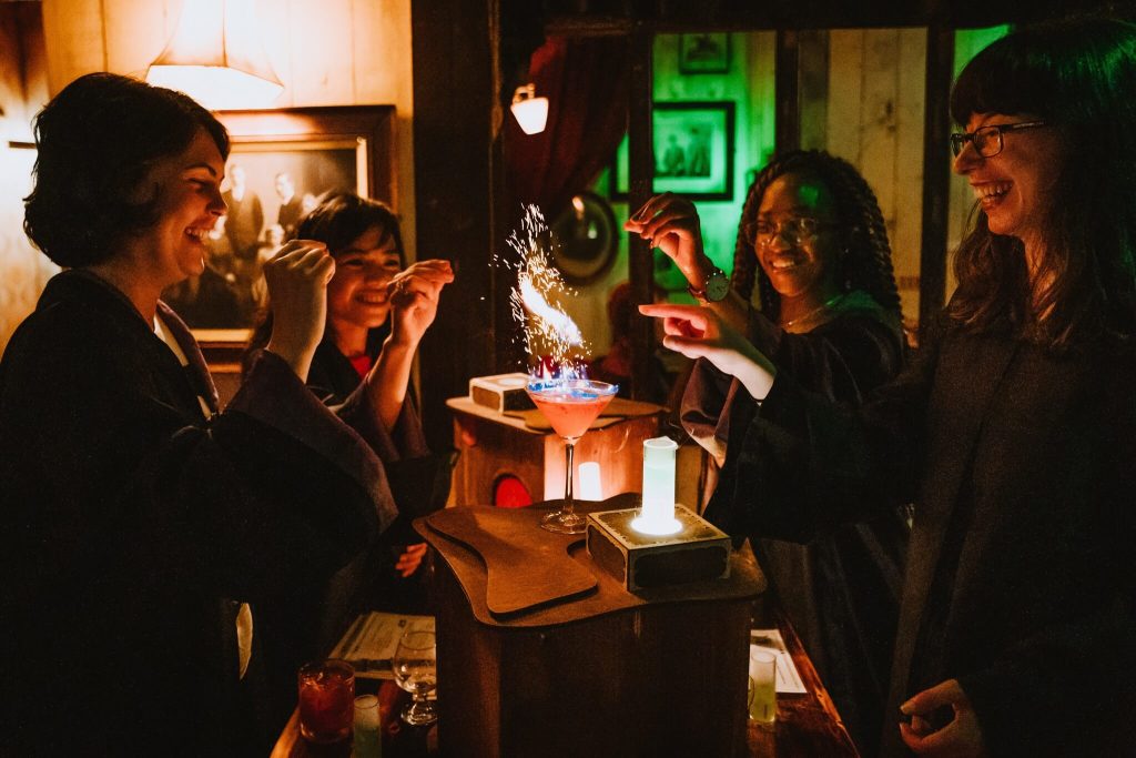 A group of friends in robes enjoying a magical cocktail experience with sparkling effects, a fun team building activity in NYC.