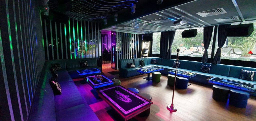 A karaoke lounge with blue seating, vibrant neon lighting, and television screens, creating a modern and inviting entertainment space.