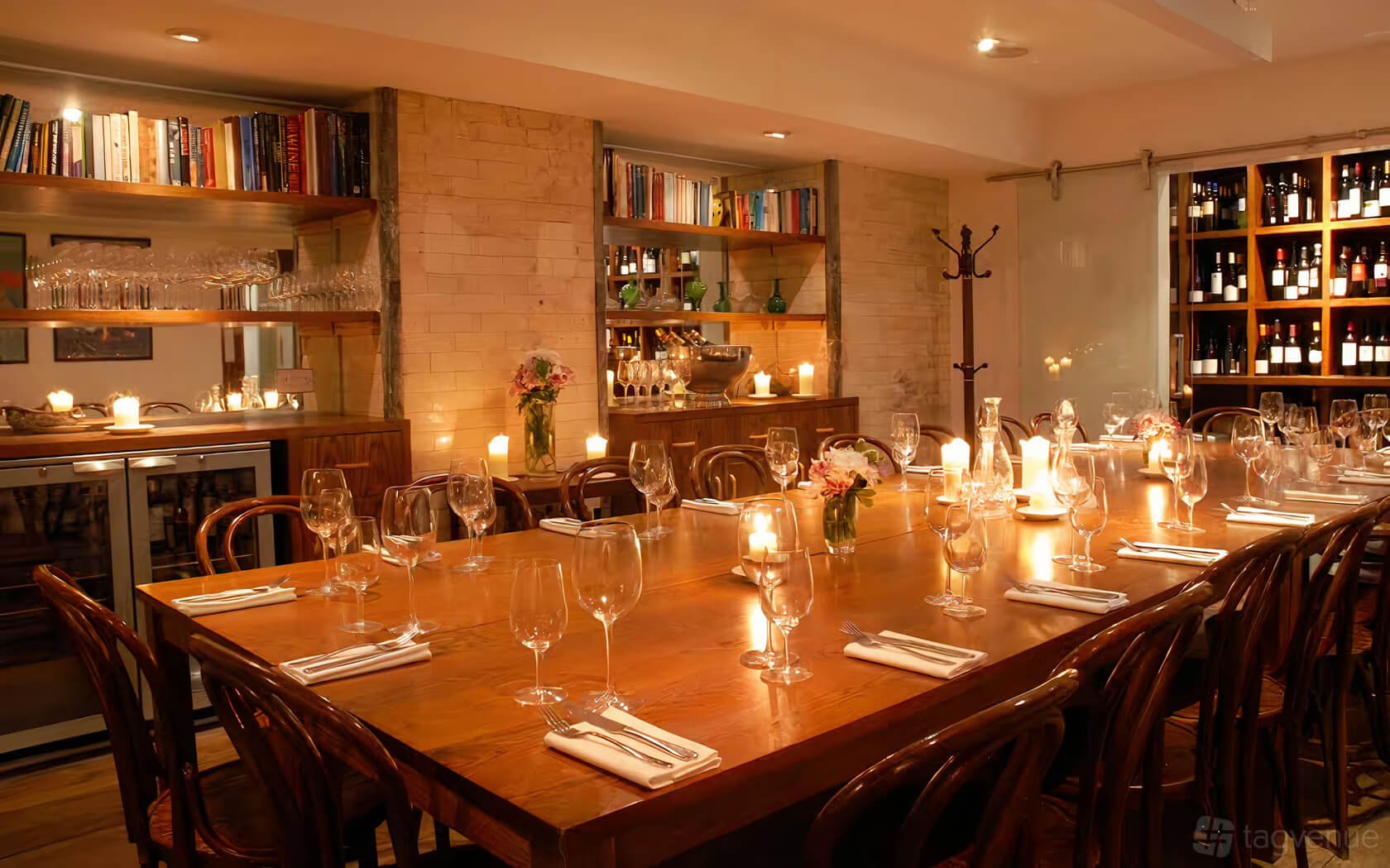 Private dining room with wine bottles exposed and a long wooden rectangular table decorated with candles and ready for dinner with forks and wine glasses.