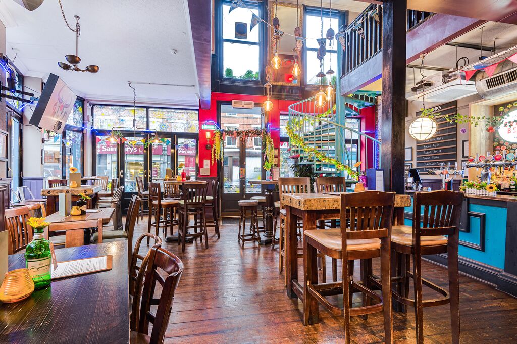A bright room with blue and red walls and wooden bar stools and high tables. The room features a bar decorated with ferns.