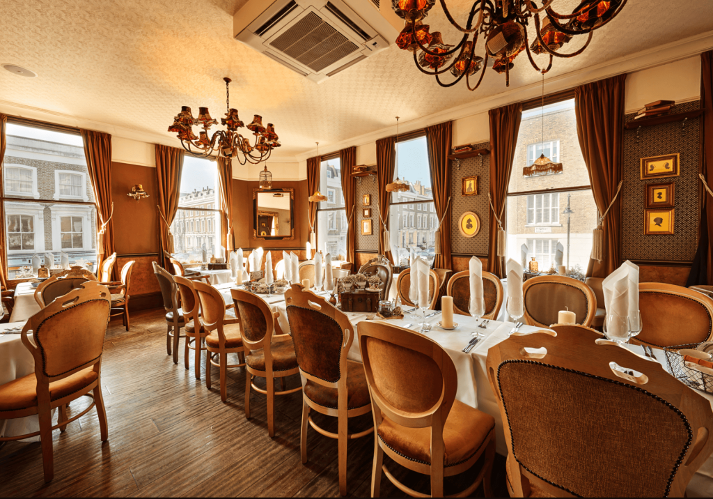 Upholstered dining chairs neatly stacked against each other with a long table set up with forks, glasses, and candles. 