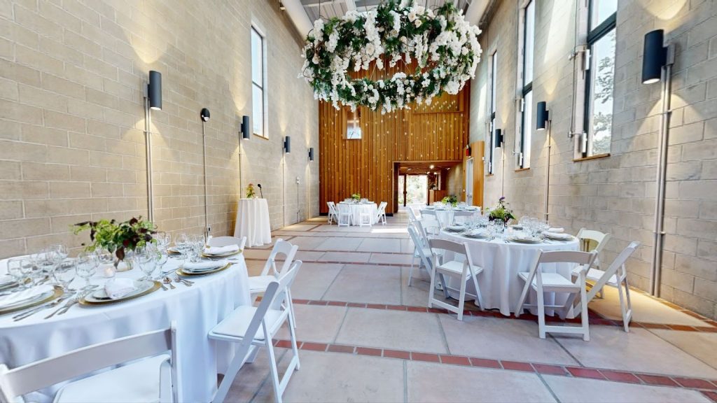 Wedding hall with rustic wooden entrance, round white tables and a chandelier made of flowers.