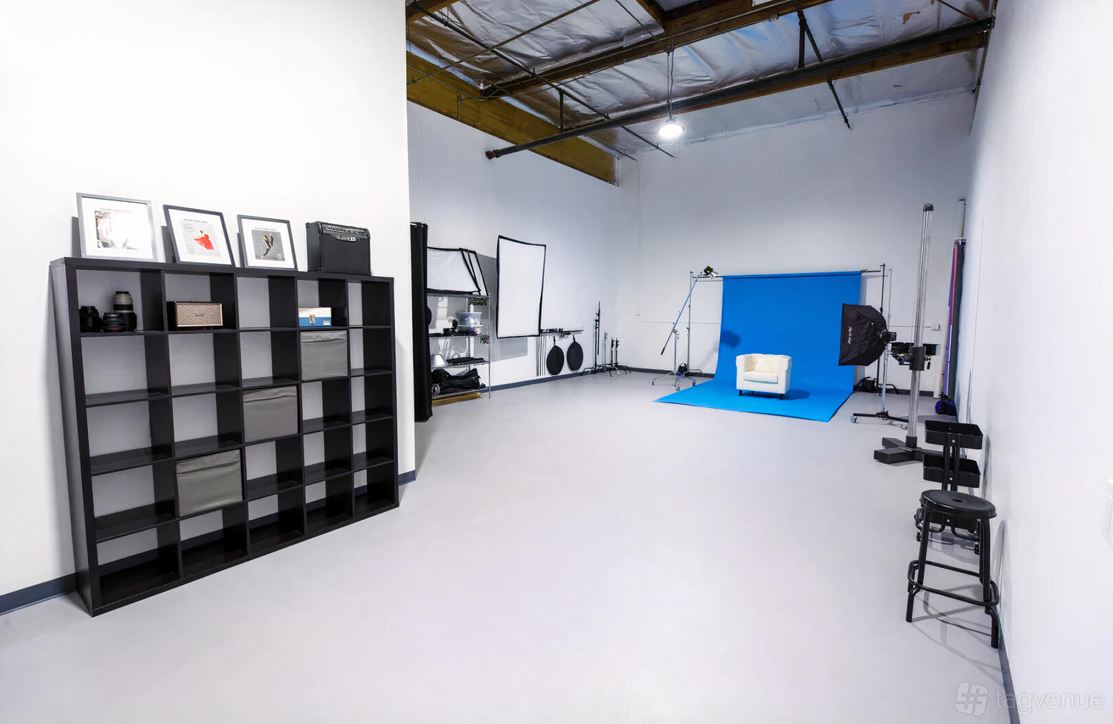 A photo studio with a blue backdrop, white armchair, studio lighting, and open shelving at Justin Morton Studio.