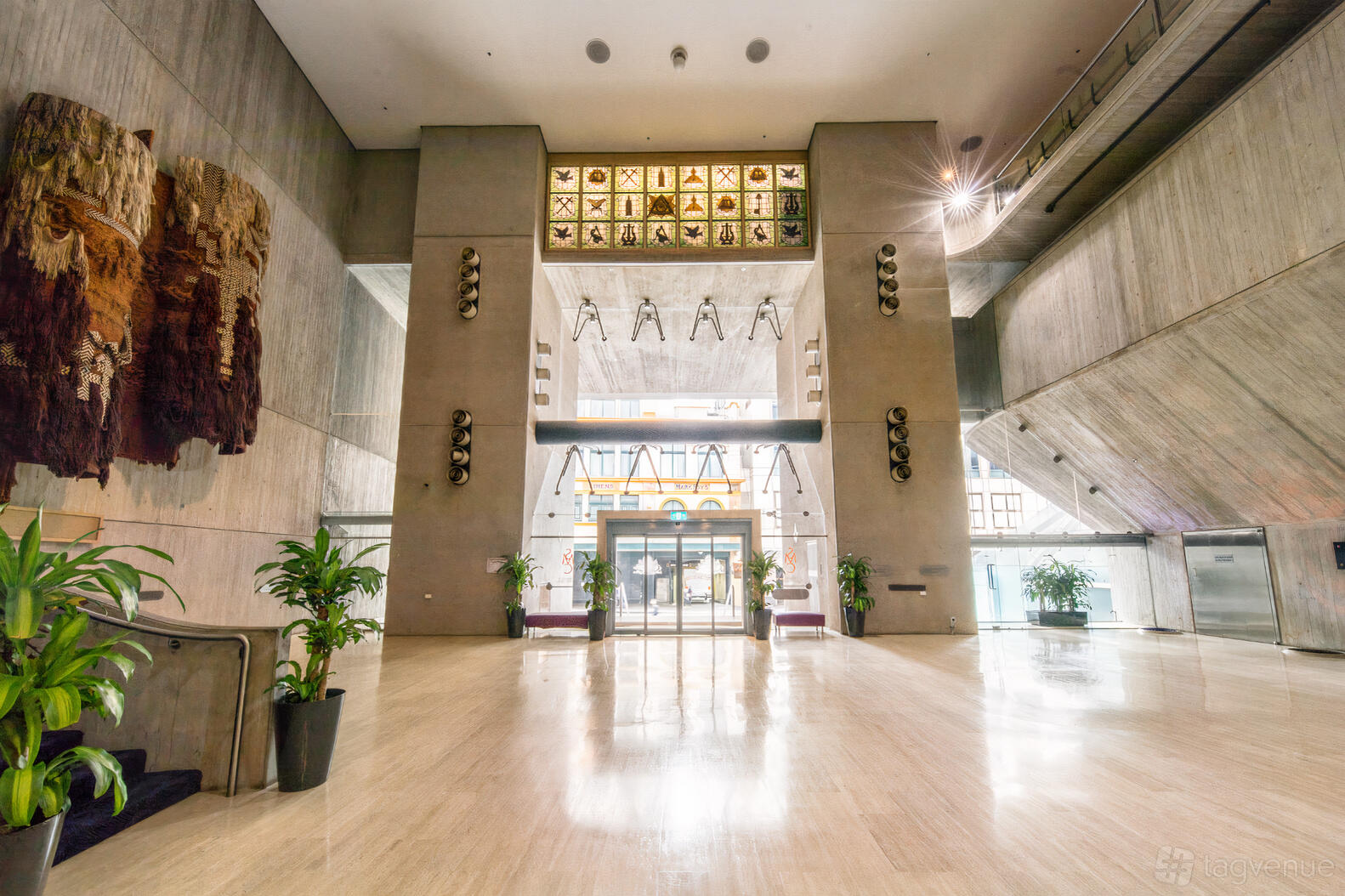 A conference centre entryway with marble floors, tall concrete walls, wall art, and potted plants at Sydney Masonic Centre.