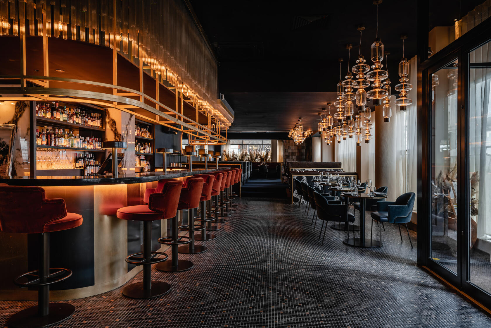 A restaurant bar with a curved illuminated counter, red velvet bar stools, and pendant lighting at Gaucho Newcastle.
