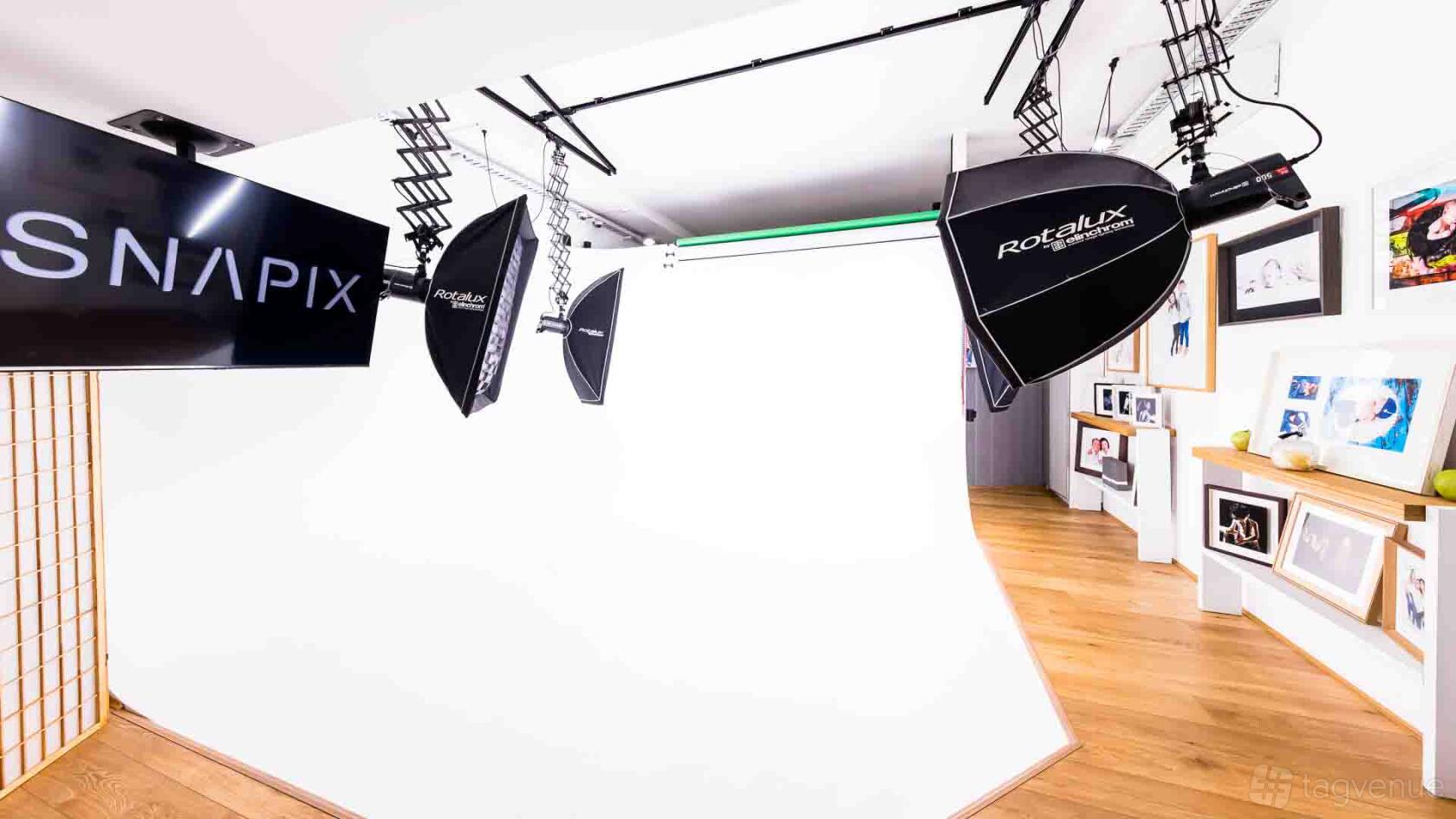 A photo studio with a seamless white backdrop, studio lights, and framed prints on wooden floors at Snapix.