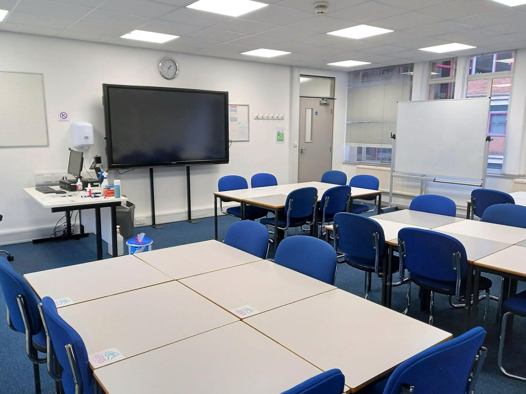 An academic event space with blue chairs, grouped tables, a large display screen, and whiteboard at University of Law - London Bloomsbury.