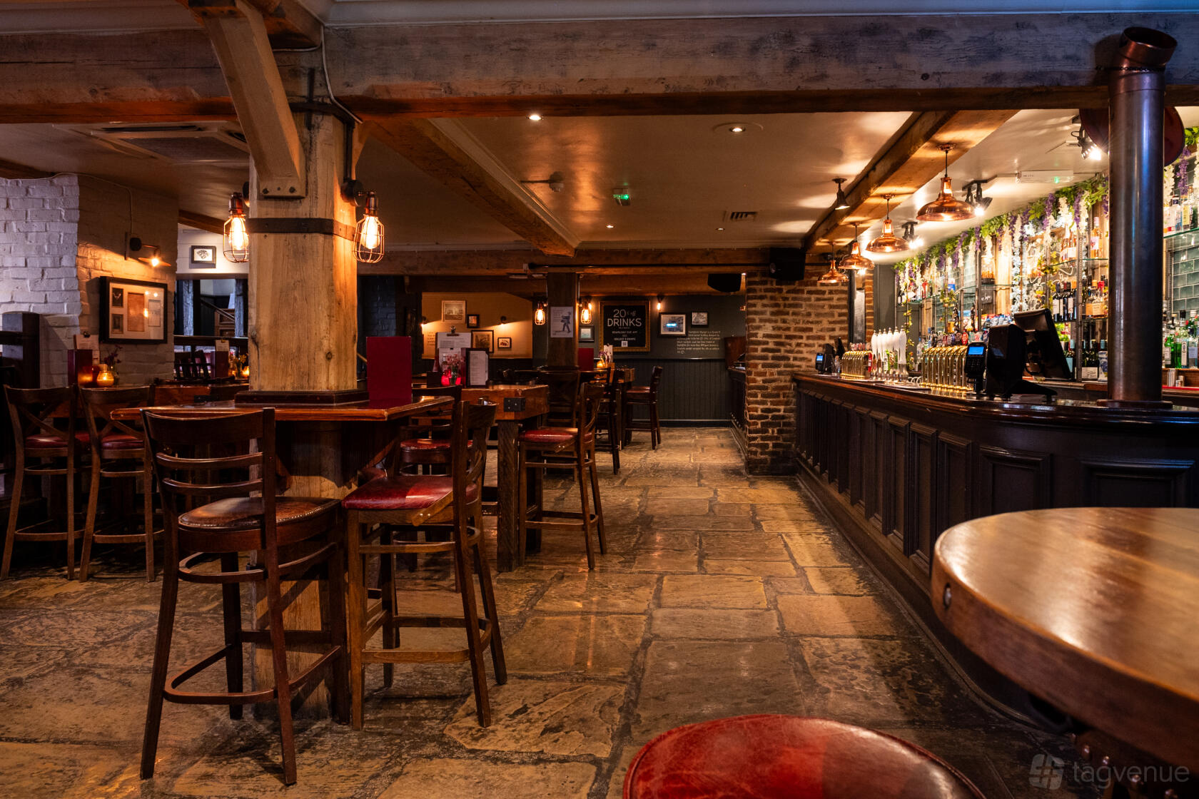 A pub with wooden beams, stone flooring, and a long bar with hanging lights at Sir Christopher Hatton.