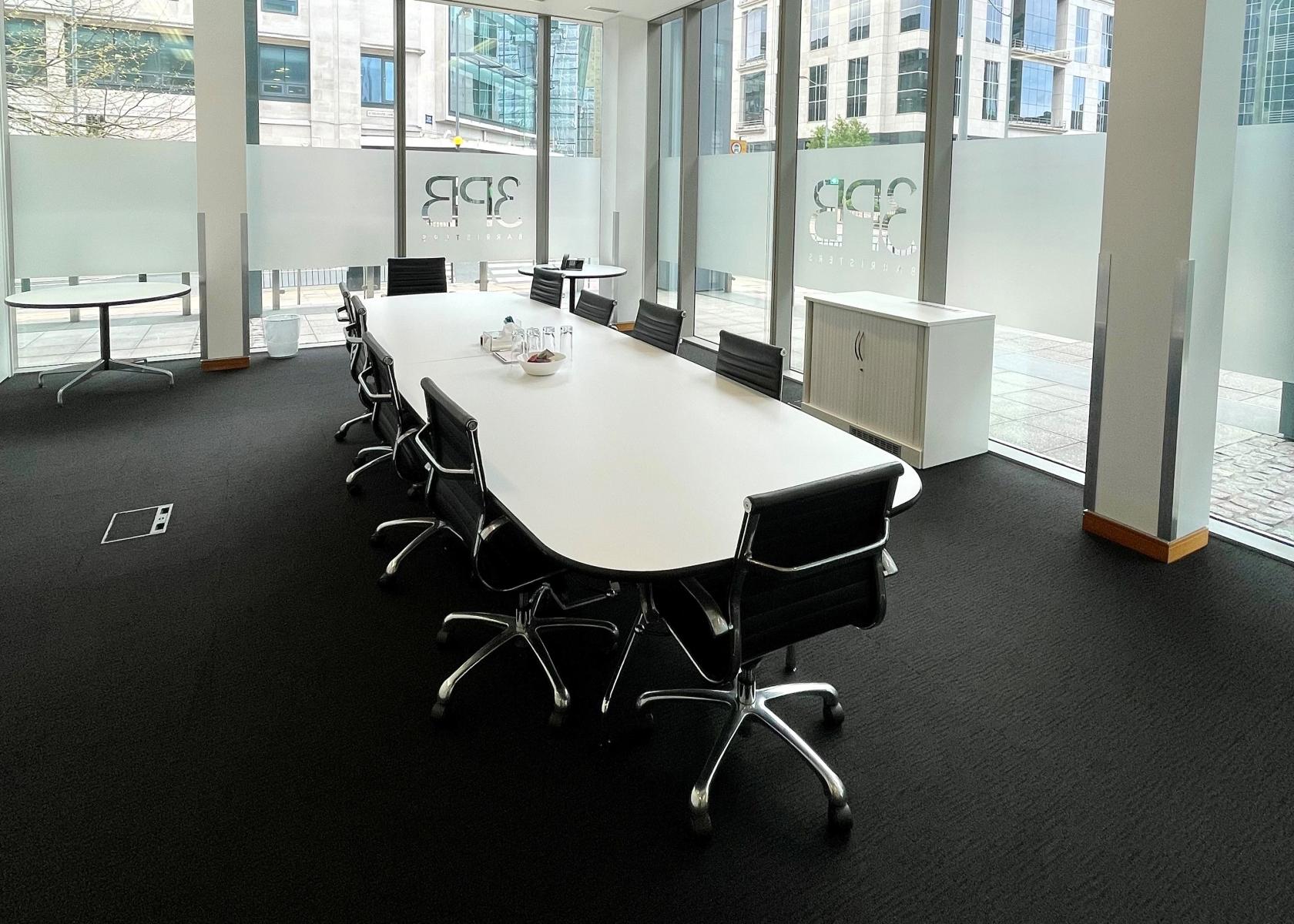 A meeting room with a long white conference table, black chairs, and floor-to-ceiling windows at Event Space at 3PB Birmingham.
