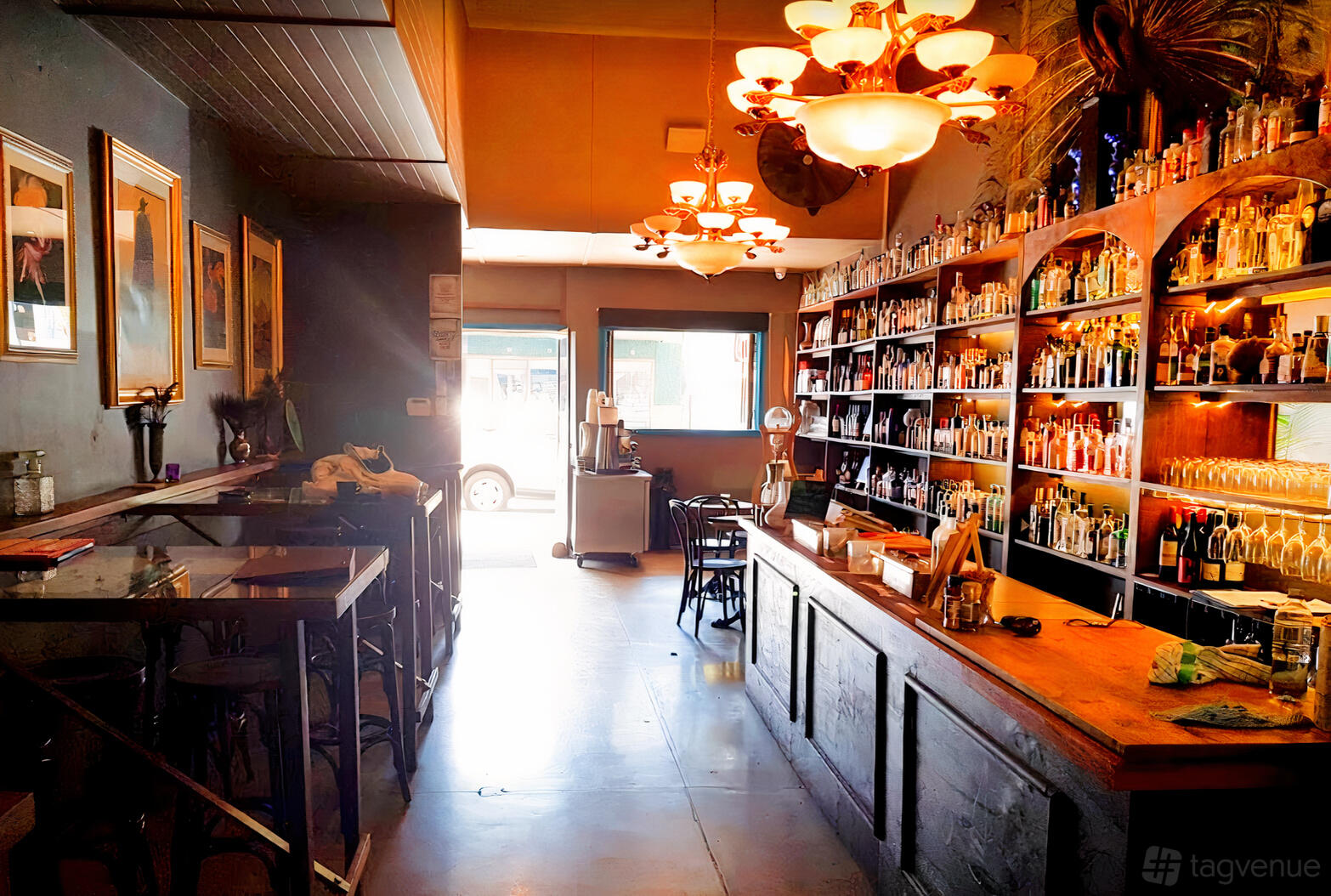 A bar with wall-to-wall shelves of liquor bottles, wooden counter, and vintage chandeliers at Proud Henry - Wine Bar and Ginoteca.