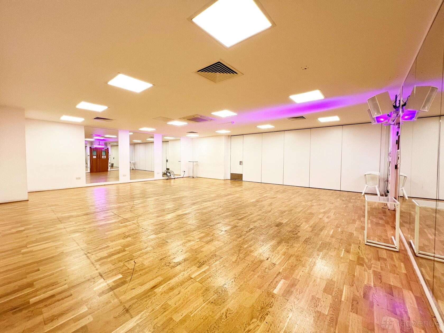A dance studio with wooden floors, full-length mirrors, ceiling speakers, and bright overhead lighting at UNIT 3.