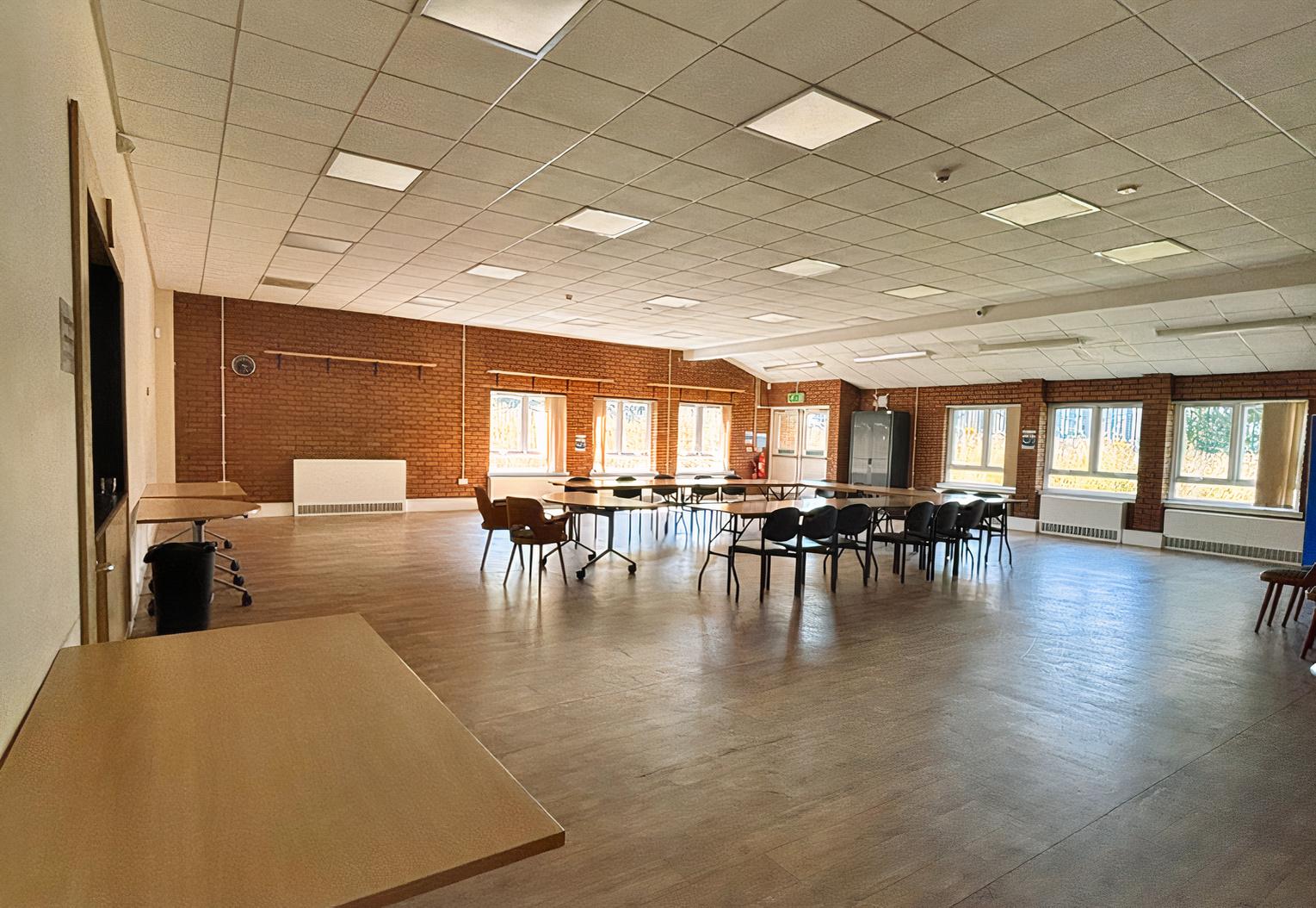 A spacious hall with wood flooring, exposed brick walls, and large windows at St. Sebastian's Community Centre.