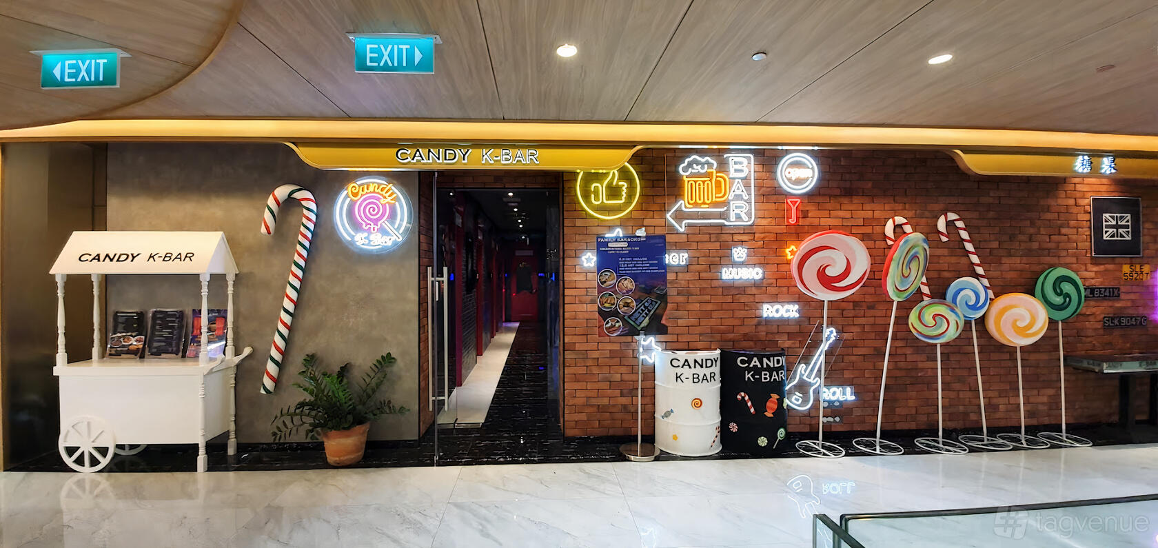 A karaoke bar entrance with neon signs, brick wall, and oversized candy decorations at Candy K-Bar Family Karaoke.