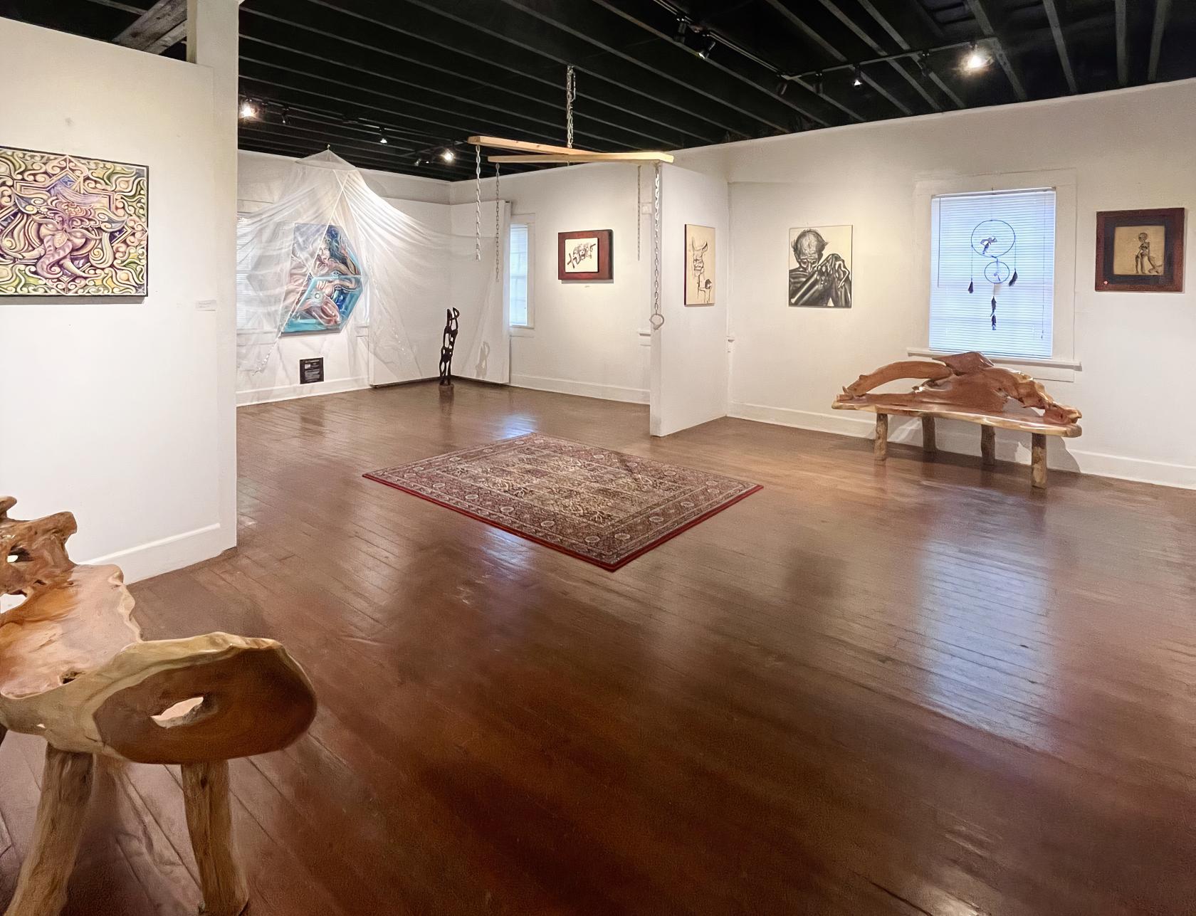 An art studio with white walls, wood floors, hanging artwork, and carved wooden benches at Healium Center.