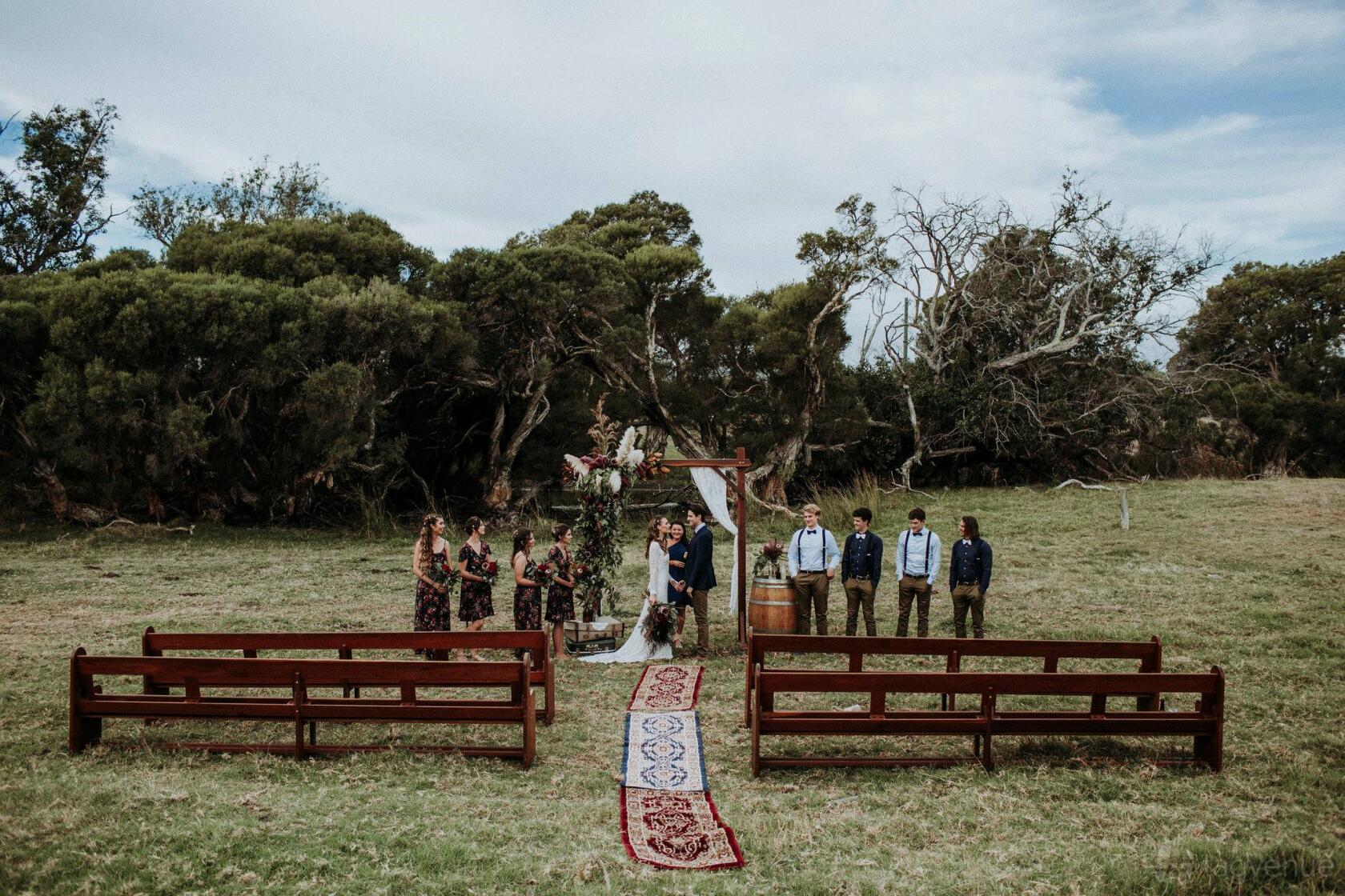 A ceremony area with wooden benches, a rug-lined aisle, and a floral archway on the lawn at Fairlawn Estate.