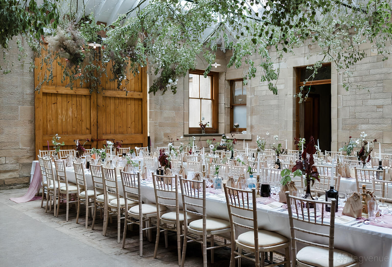 A historic building with stone walls, tall windows, and banquet tables decorated with florals at Cambo House & Estate.