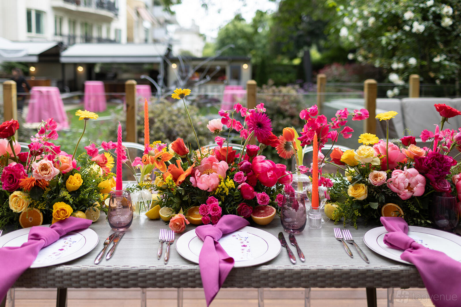 A garden event venue with a long table decorated with bright floral centerpieces and pink napkins at Six Park Place.
