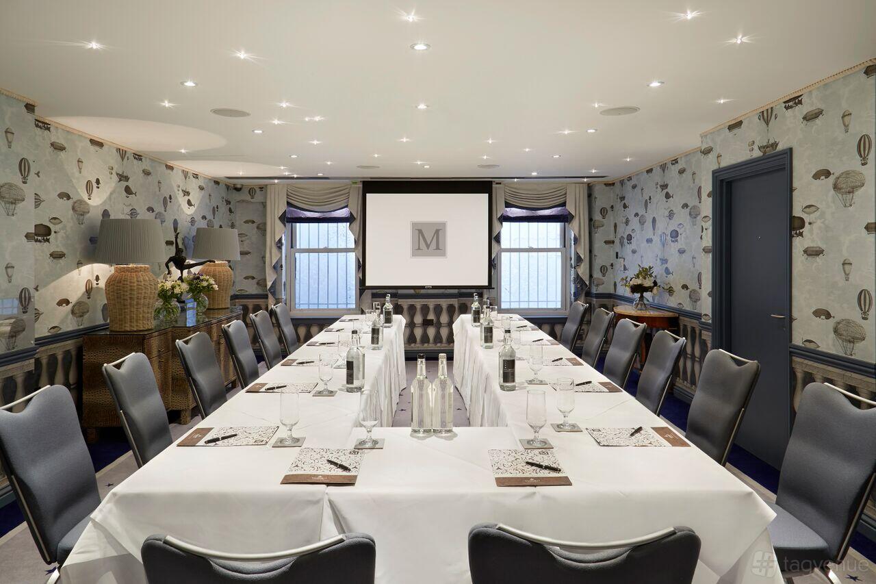 An event space with U-shaped conference tables, patterned wallpaper, and a projector screen at The Mandeville Hotel.