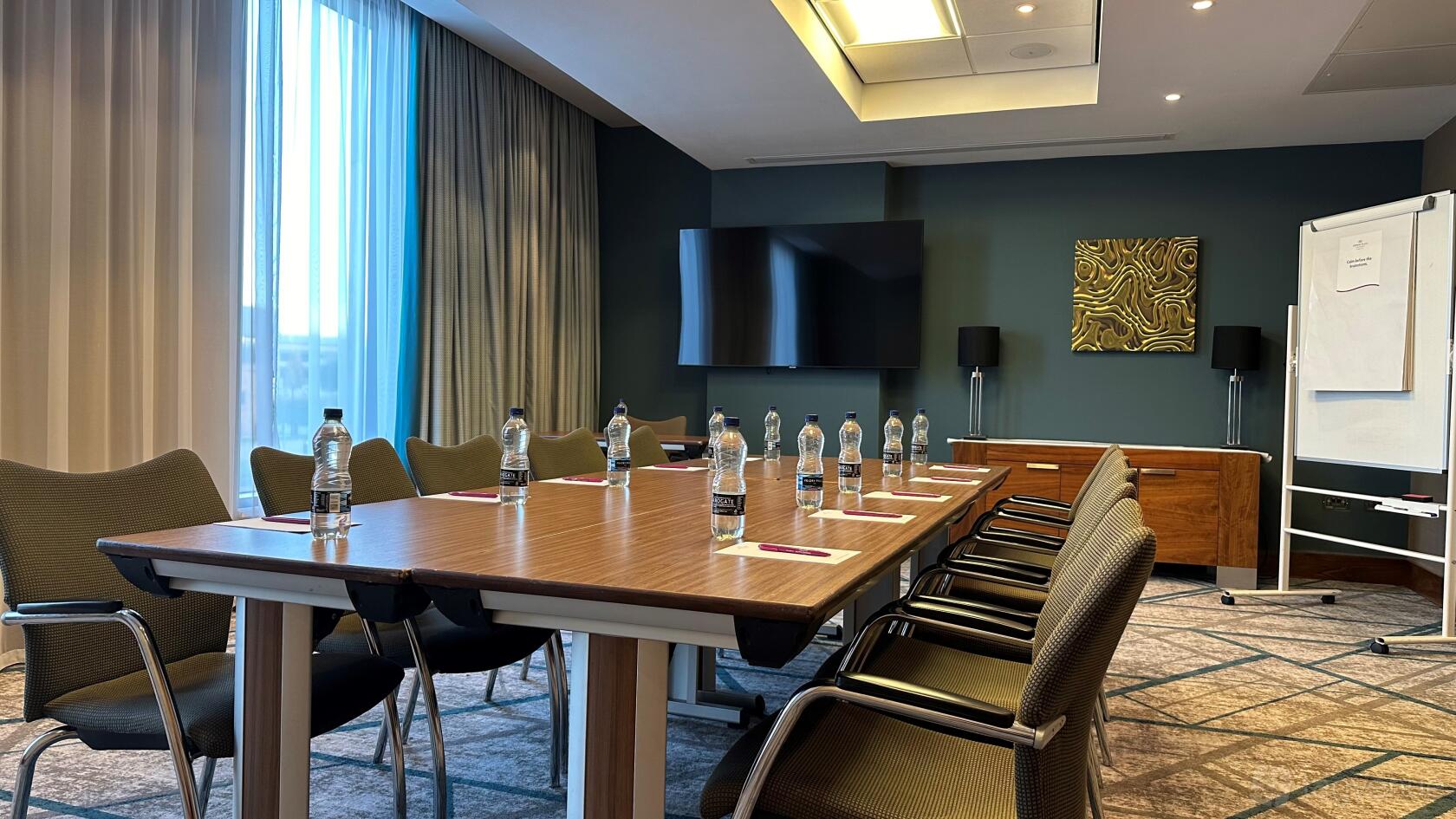 An auditorium conference room with a long wooden table, bottled water, and a wall-mounted screen at Crowne Plaza Reading.