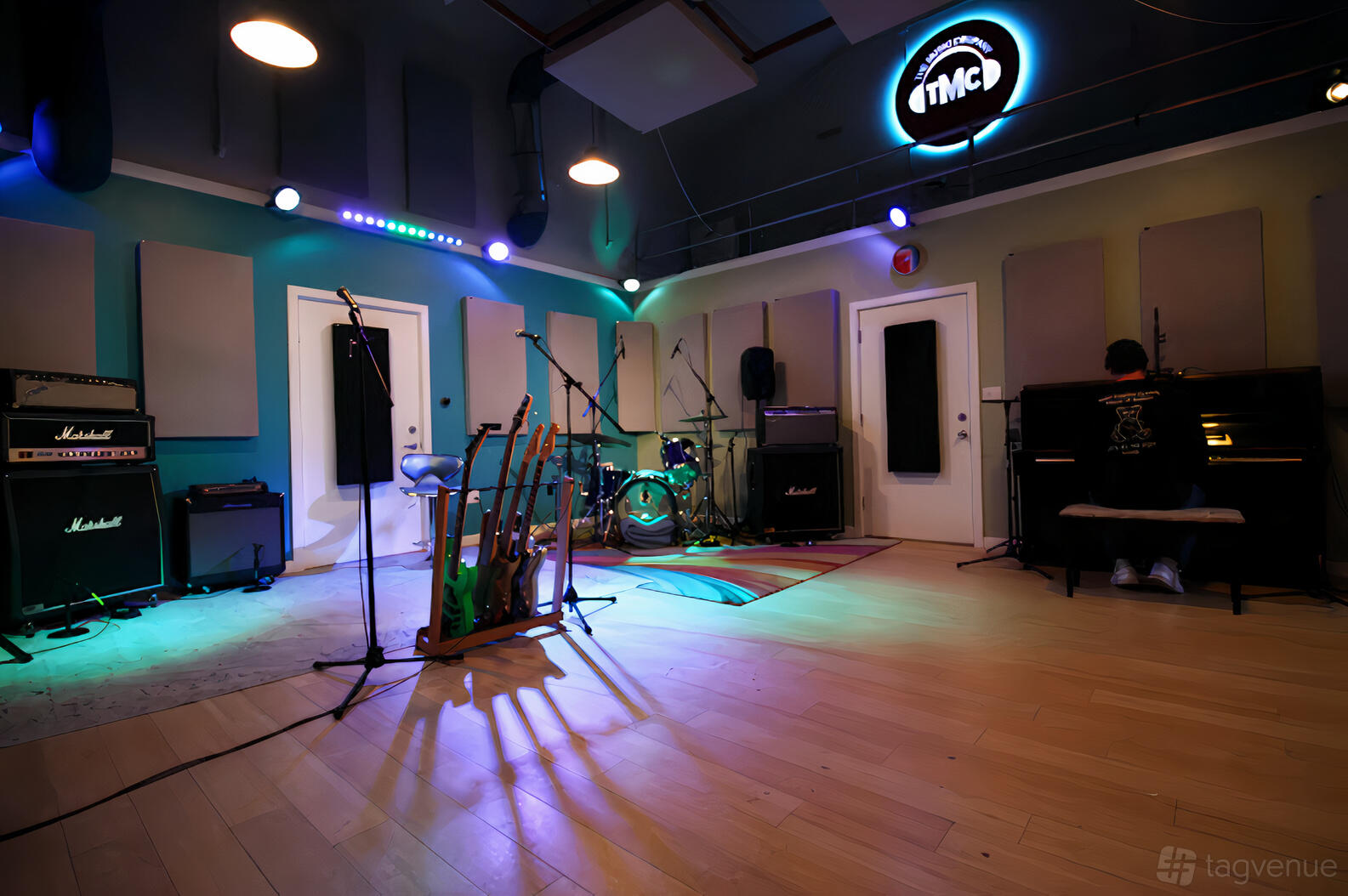 A rehearsal studio with drum kit, guitar stands, amplifiers, and acoustic wall panels at The Music Company.