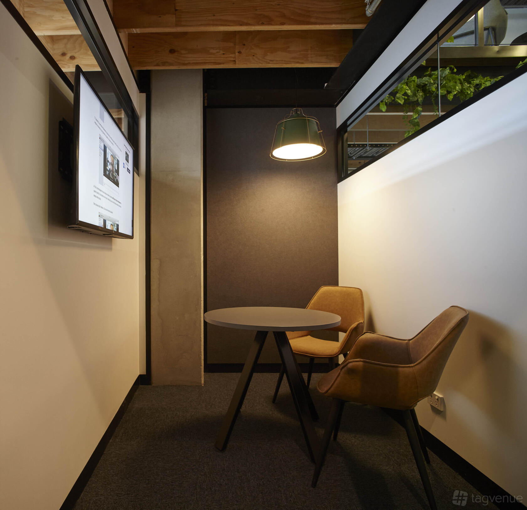 A meeting room with two tan chairs, a round table, a wall-mounted screen, and pendant lighting at collective_100.