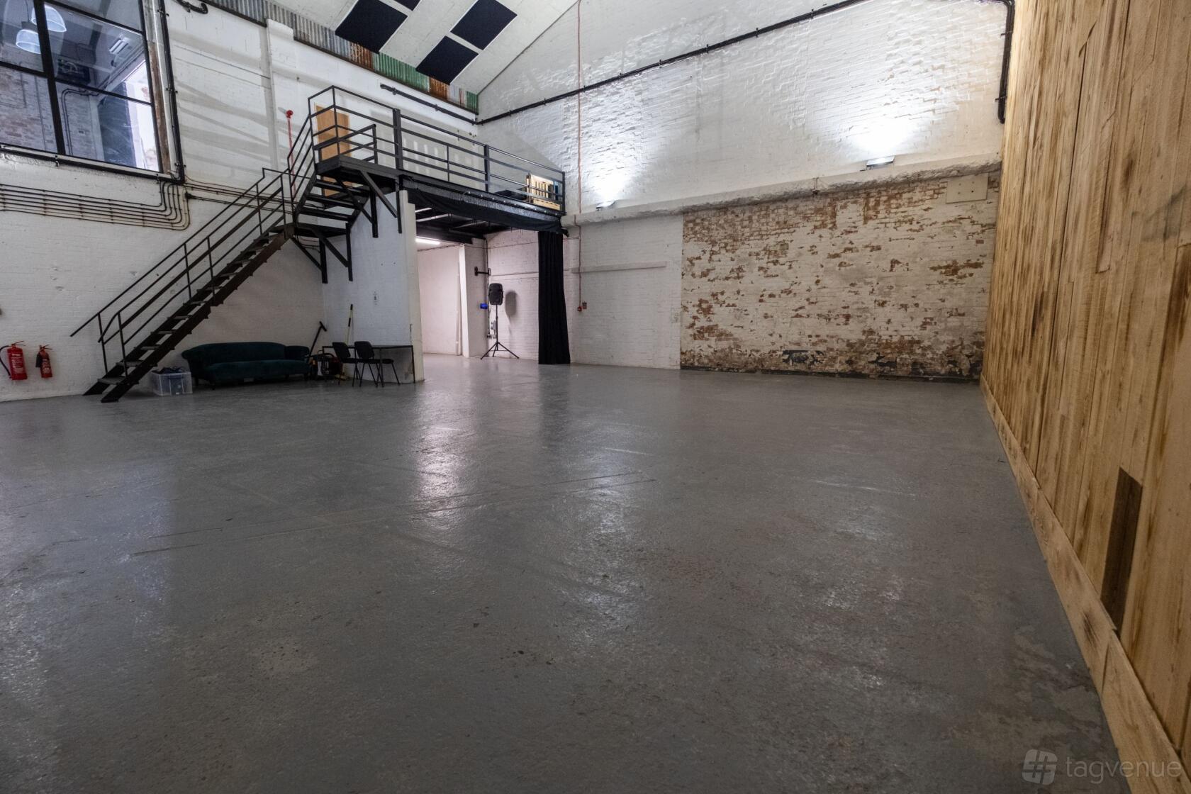 A film studio with high ceilings, exposed brick walls, and a metal staircase leading to a mezzanine at Tannery Film Studios.