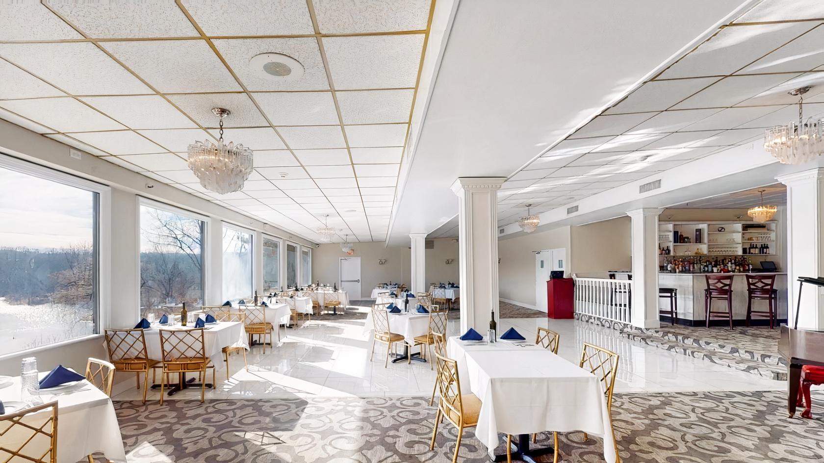 An event venue with large windows, chandeliers, patterned carpet, and set tables overlooking a lake at Jefferson on the Lake.
