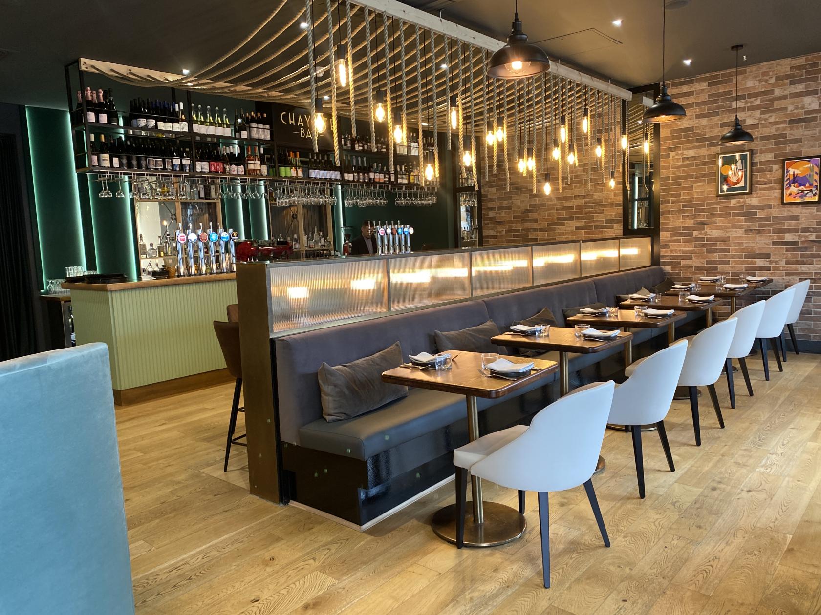 A restaurant dining area with hanging pendant lights, exposed brick walls, and a long banquette at Chayote.