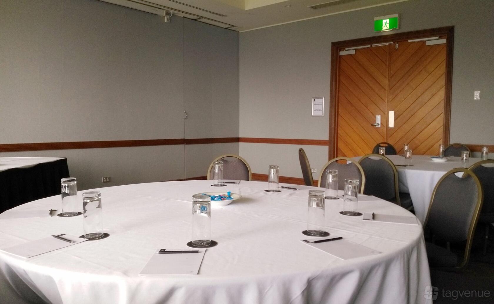 An event space with round tables covered in white linens, set with glasses, notepads, and pens at Fairmont Resort Blue Mountains.