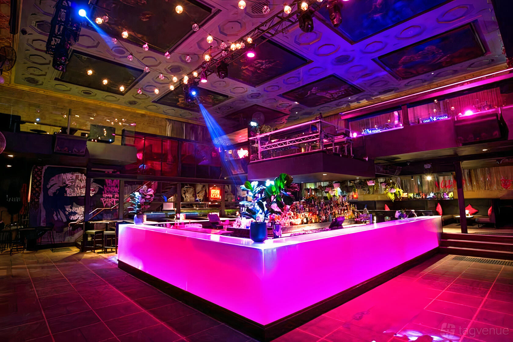 A nightclub event venue with a glowing pink-lit central bar, high ceilings, and colorful uplighting at Ms Collins.