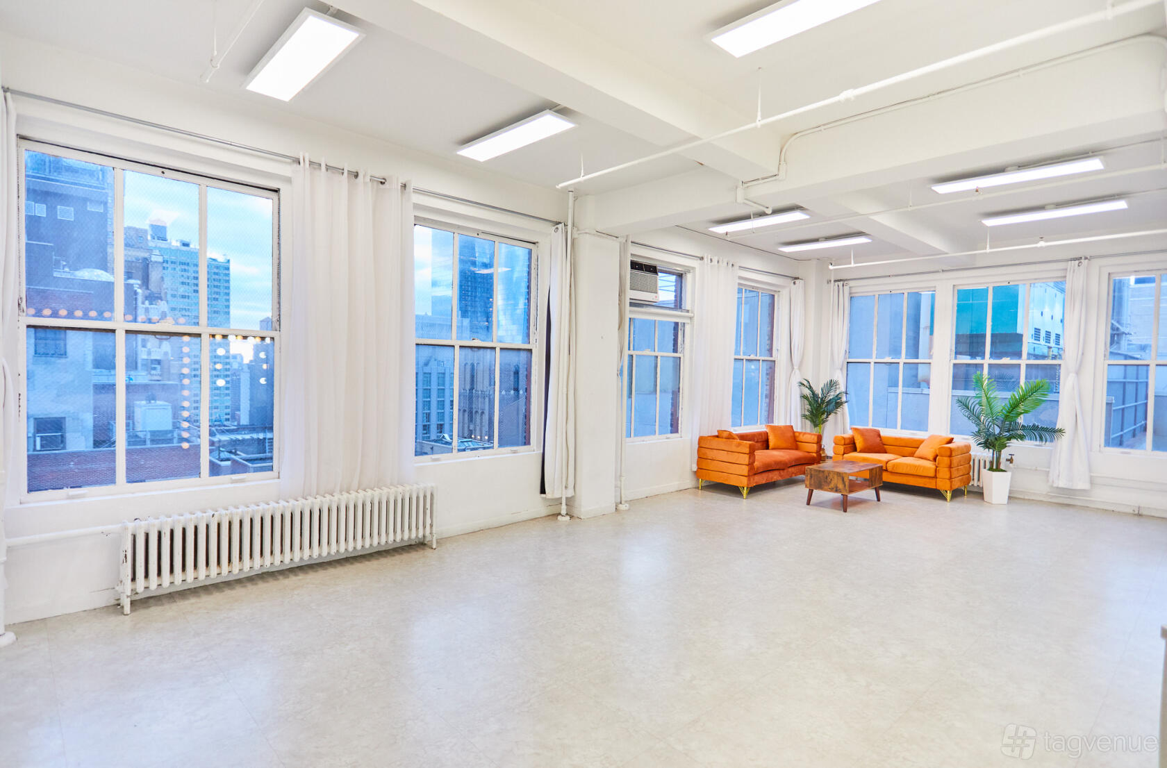 An event space in a loft with large windows, city skyline views, and orange sofas at Event Rental Space Manhattan 23rd Floor.