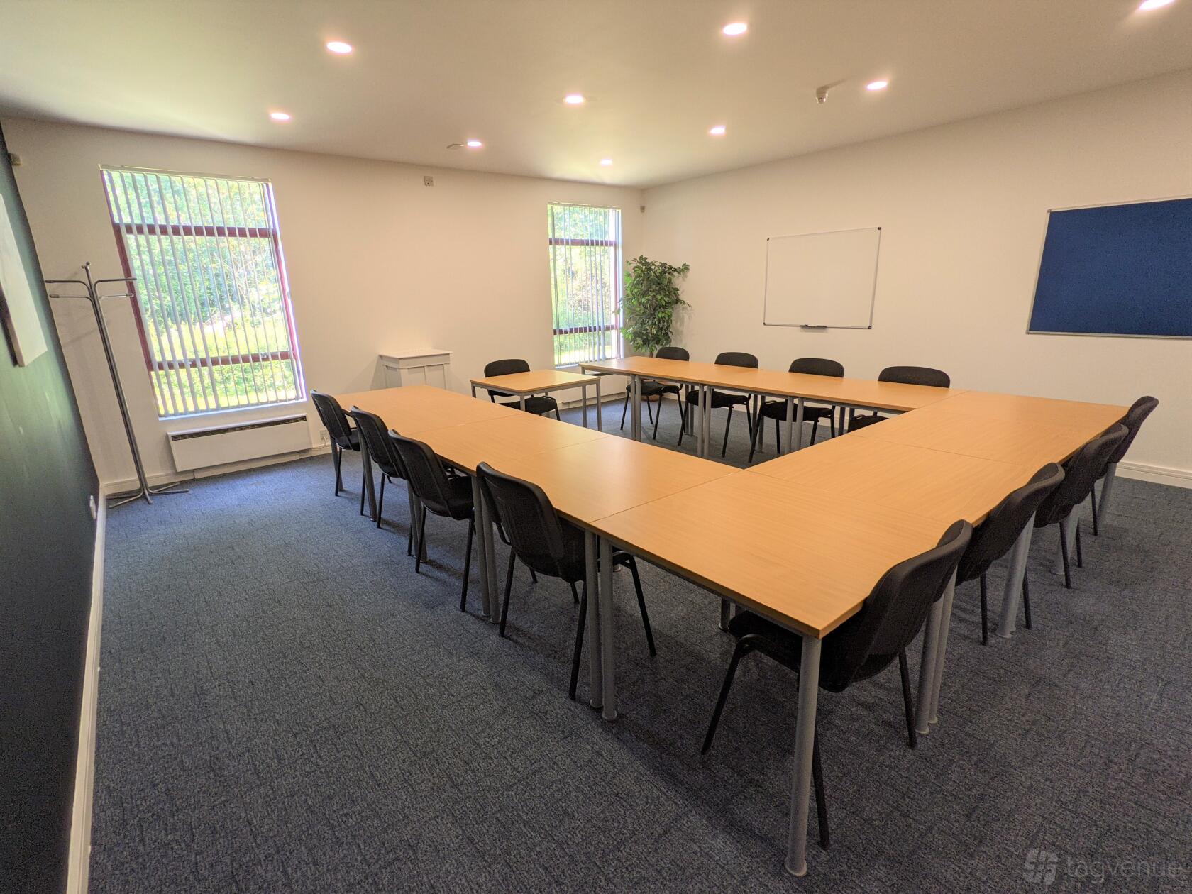 A meeting room with U-shaped tables, black chairs, large windows, and a whiteboard at Tees Valley.