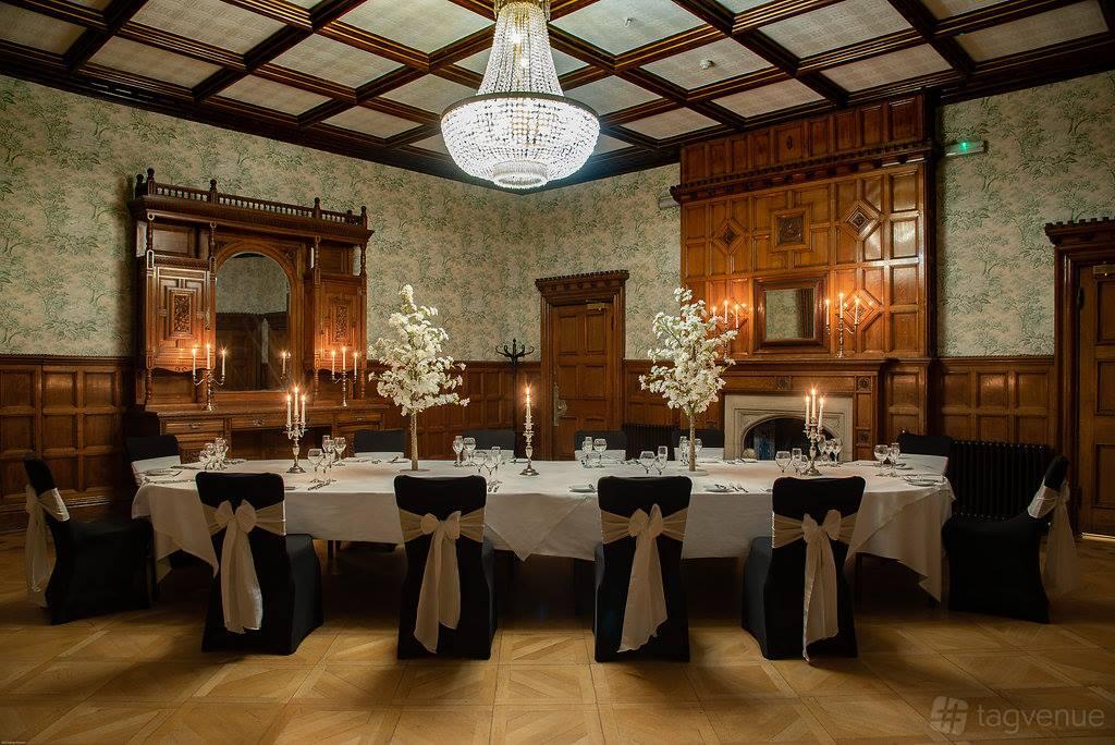 An event space with wood-paneled walls, ornate fireplace, chandelier, and oval table at Pendley Manor Hotel.