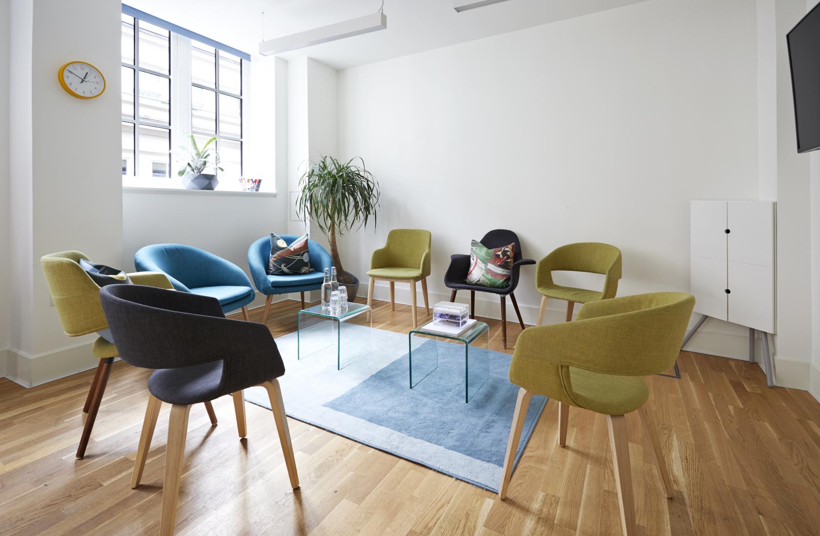 A coworking space with colorful chairs arranged in a circle, large windows, and a potted plant at Wallacespace Spitalfields.