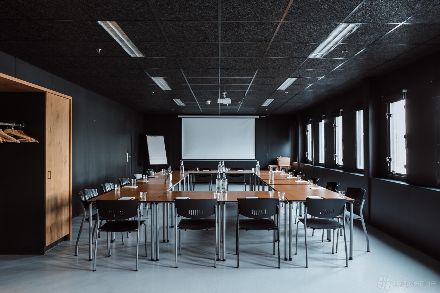 An event space with large windows, a U-shaped meeting table setup, and a projection screen at Good Hotel London.