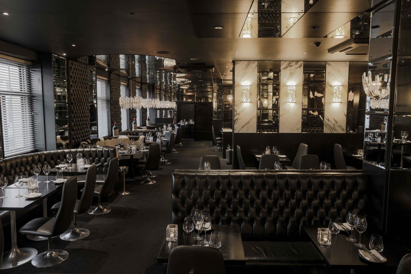 A dining room with tufted black leather banquettes, mirrored walls, and crystal chandeliers at Gaucho Piccadilly.
