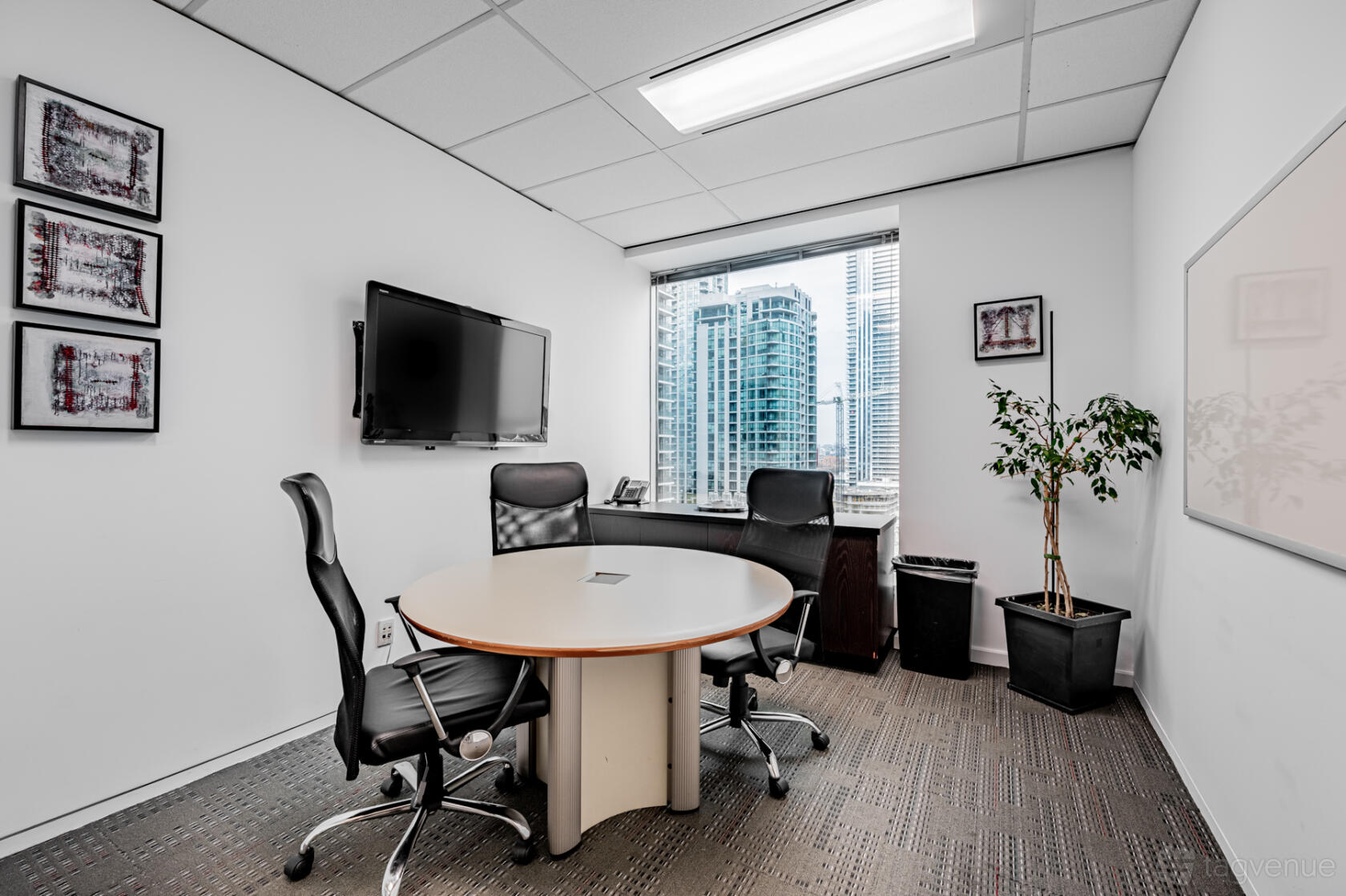 A meeting room with a round table, three office chairs, wall-mounted TV, and city views at The Rostie Group.