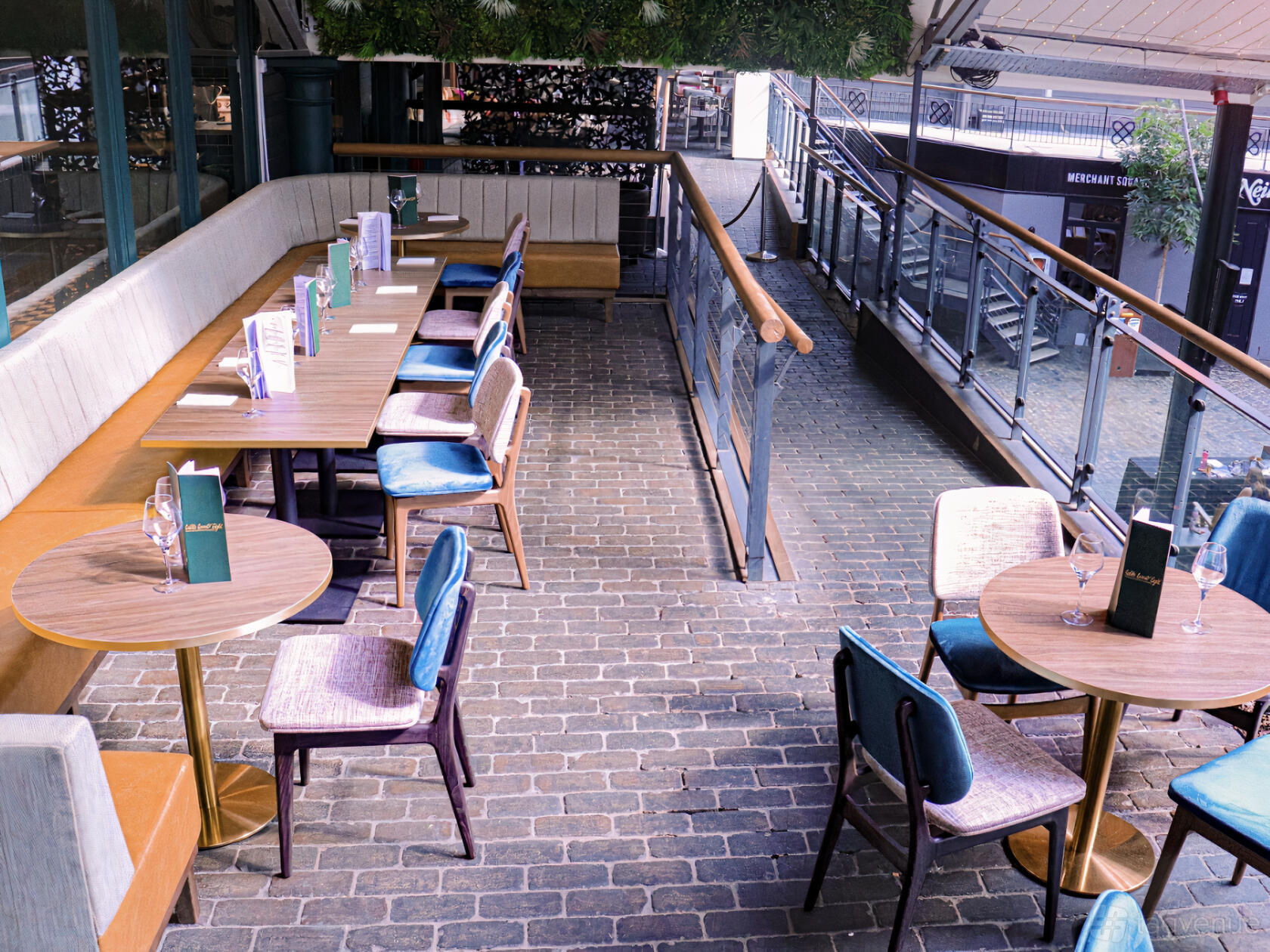 A terrace at a restaurant with brick flooring, cushioned banquette seating, and outdoor tables at Table Twenty Eight.