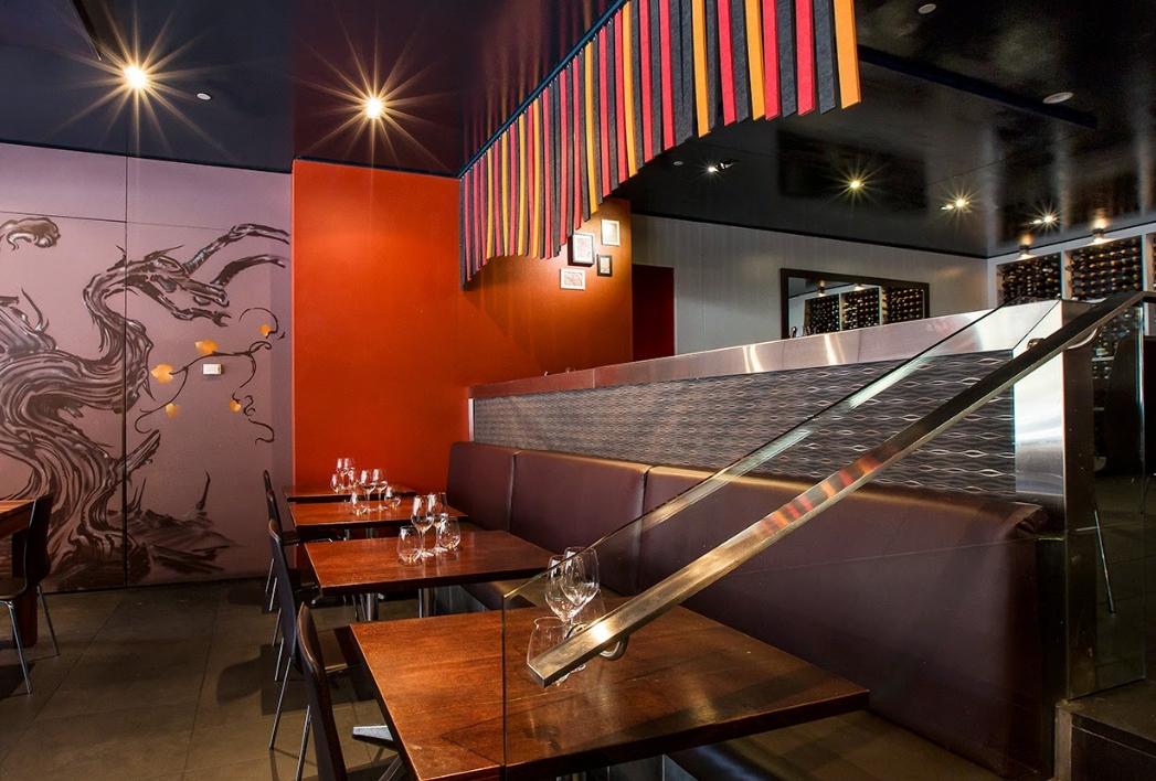 A bar with dark wooden tables, red accent walls, and a wall mural at Fix Wine Bar + Restaurant.