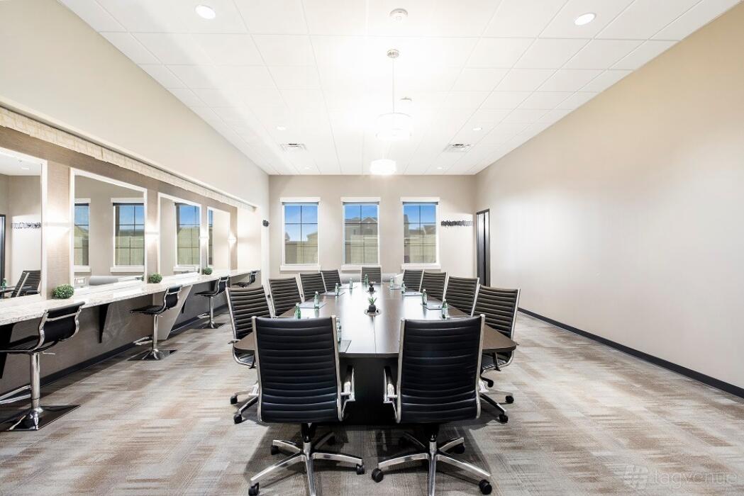 A boardroom with a long black table, modern black chairs, bright lighting, and large windows at The Venue.