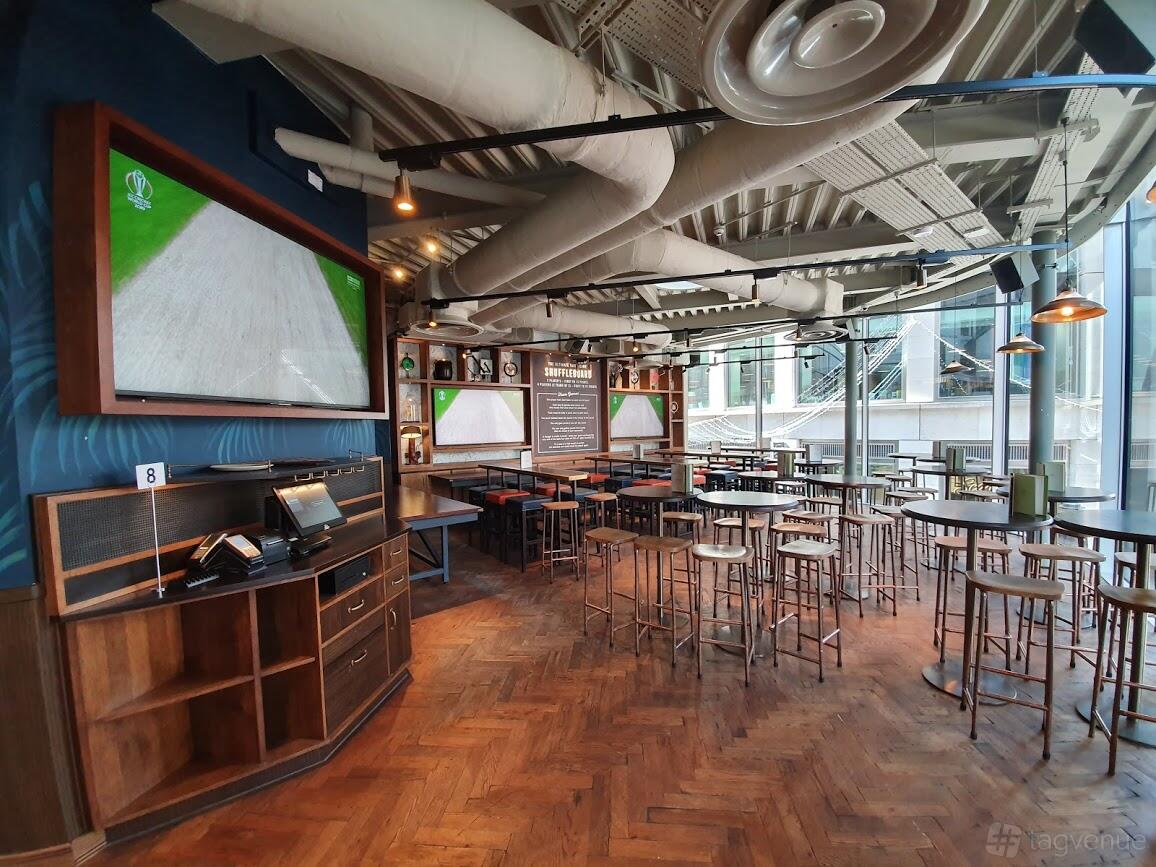An event space in a pub with large windows, parquet flooring, and high tables at Broadwood.