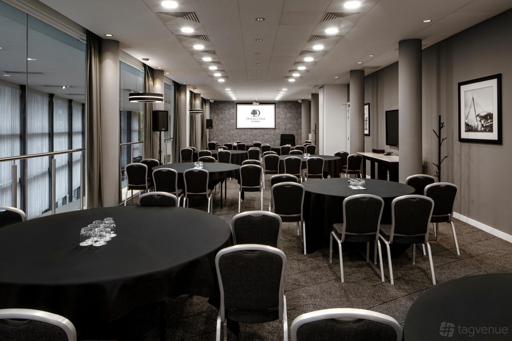 A hotel meeting room with round and theater-style seating, black tablecloths, and a projector screen at DoubleTree by Hilton Manchester - Piccadilly.