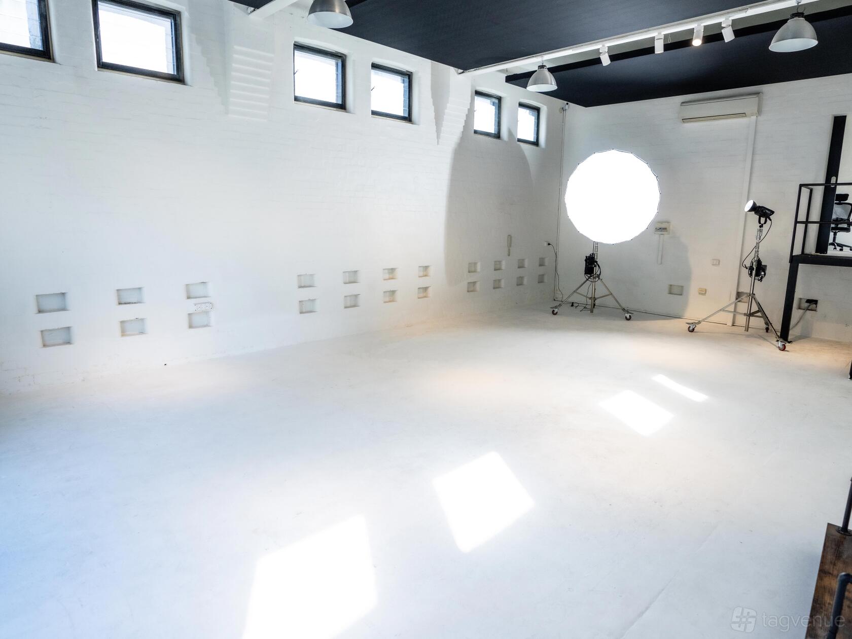 A photo studio with white brick walls, high windows, and a large studio light at The Media Joint.